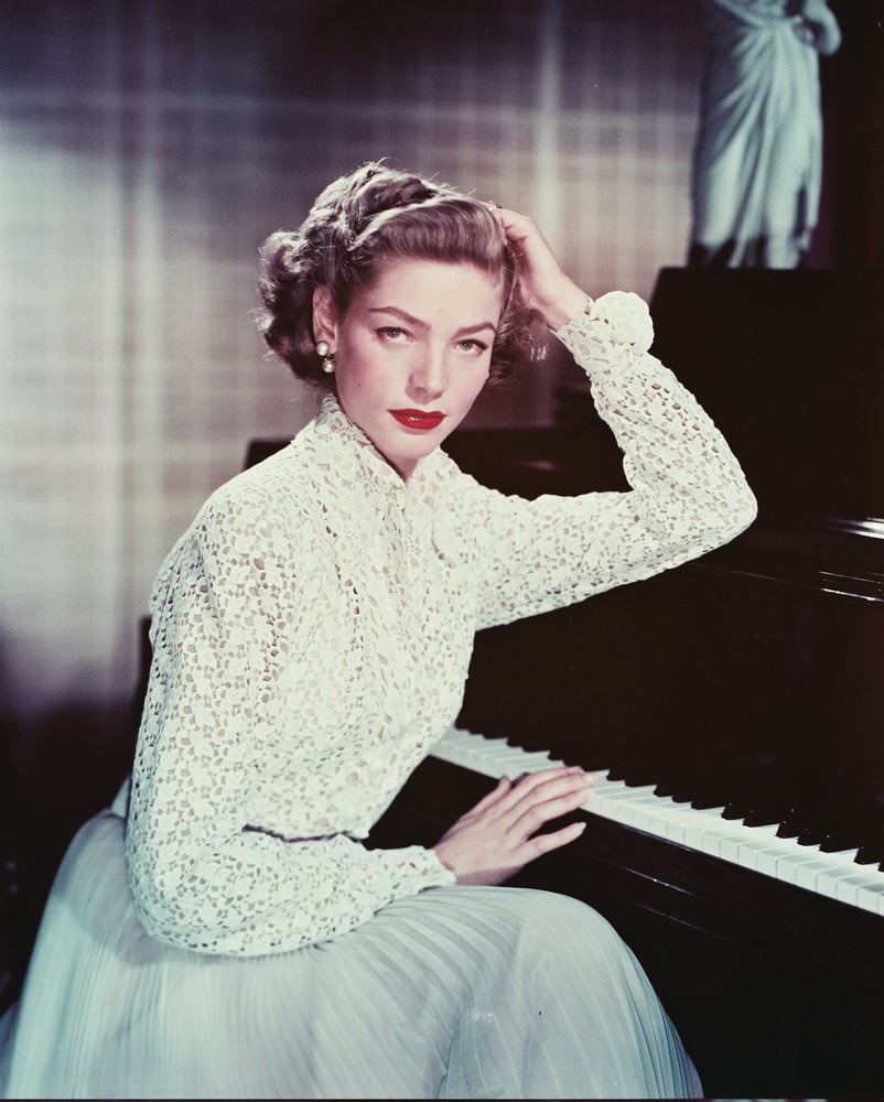 Posing beside a piano in a macrame blouse and light blue pleated skirt, 1955.