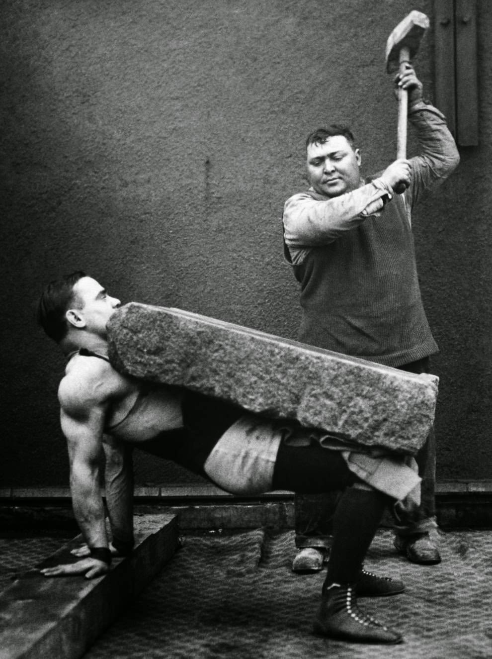 Man crushes a block placed on the stomach of a strongman, 1930
