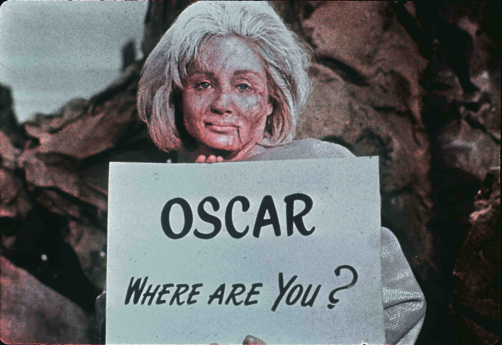 An historic and previously rarely seen shot of Susan Oliver in fully deformed state makeup and costume holding a sign with an inside joke directed towards Desilu executive Oscar Katz.