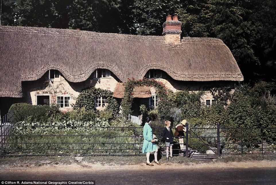 Two children and a lady stand outside of a thatch-roofed cottage in Hampshire in 1931