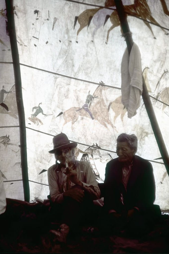 Two Native American men smoke a pipe in their teepee at the campgrounds.