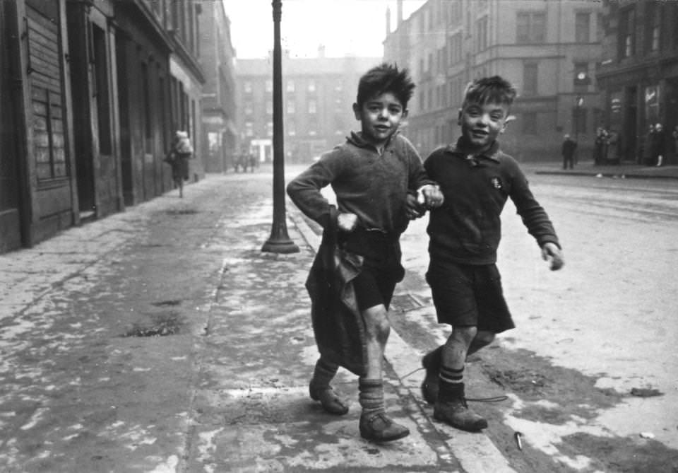 Two young boys link arms as they walk down the street in the Gorbals