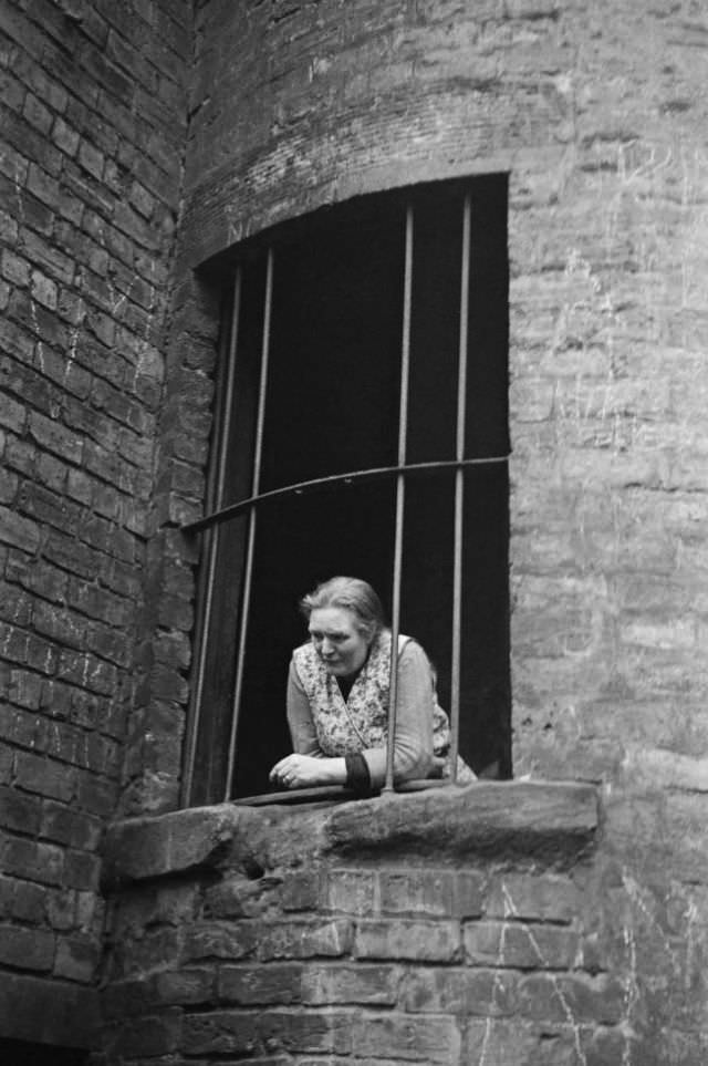 A woman peers out of the window of her tenement