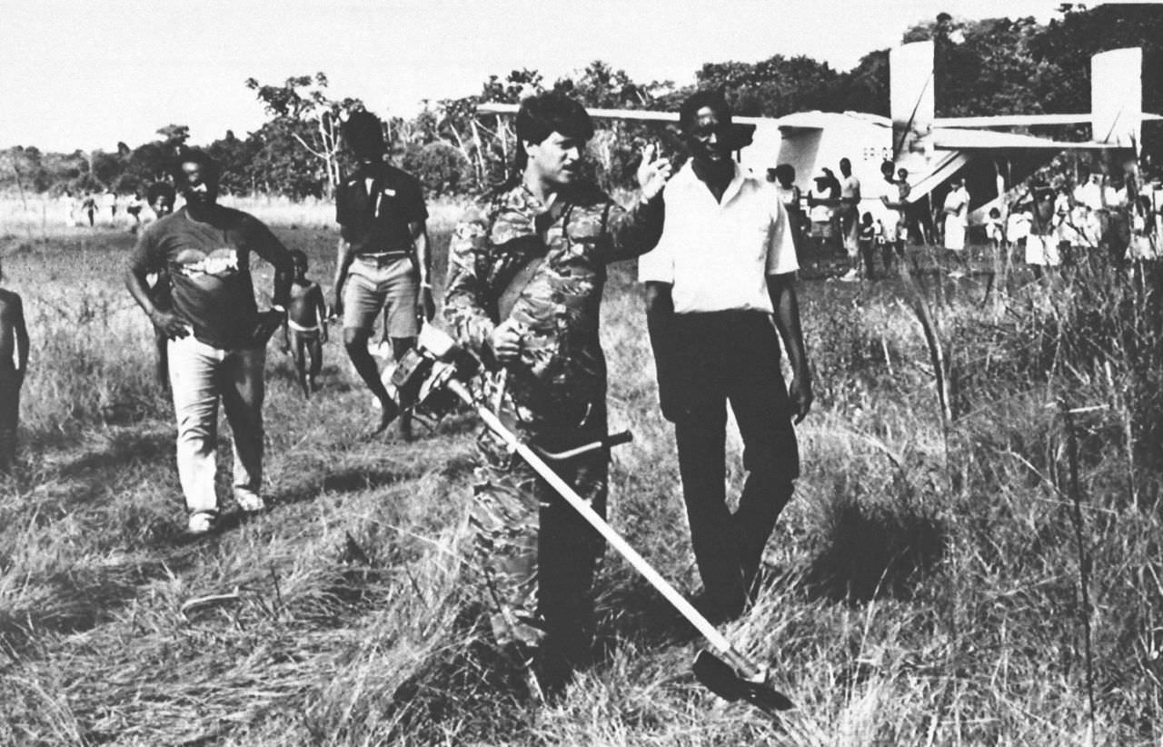 Villagers look on as Capt. Gerry Gouveia, a commercial pilot, directs grass-clearing at the remote airstrip where gunmen ambushed and killed U.S. Rep.