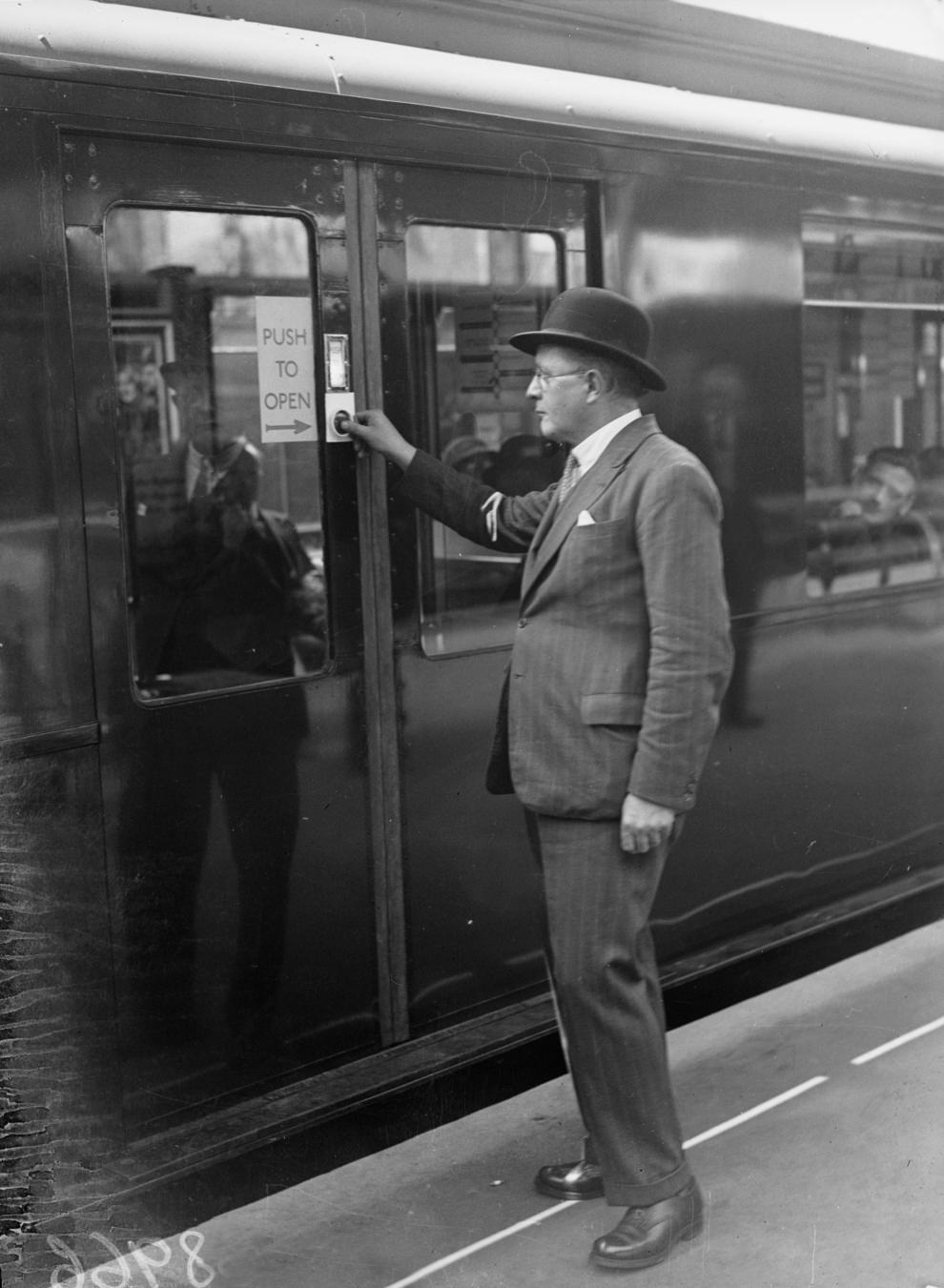 A passenger opening one of the doors on the Hammersmith and City Underground Line, which have been fitted with new buttons for opening and closing doors, 1936.