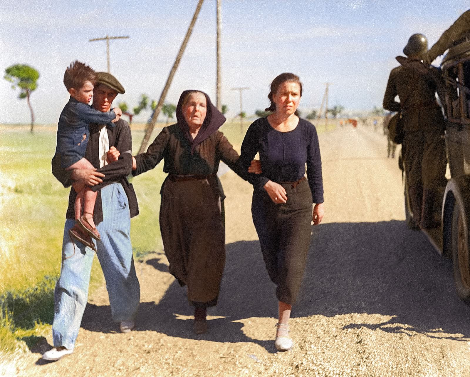 A family of Belgian refugees hold and support each other as they pass a military vehicle while walking the road to France, circa 1940. Behind them are other groups of refugees fleeing occupied Belgium.