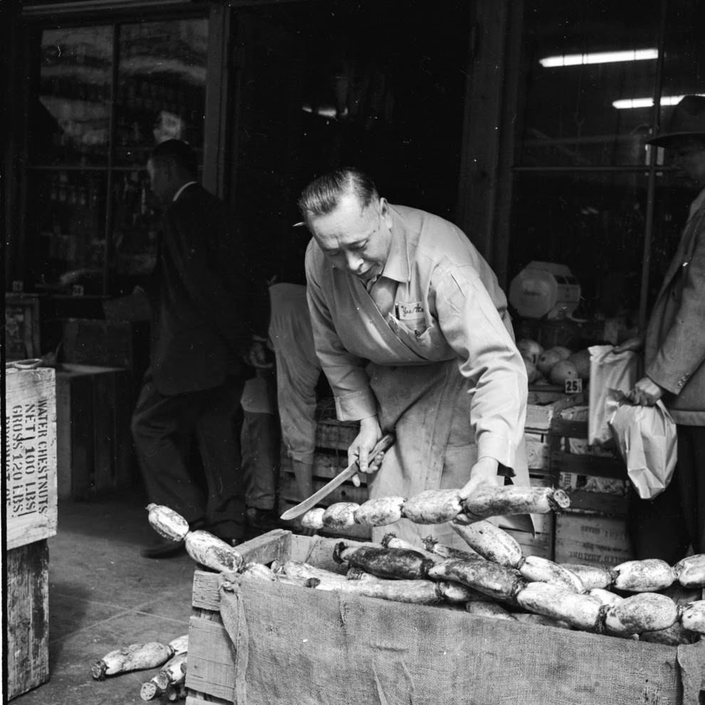 A vendor slices off a chunk of lotus root for a customer.