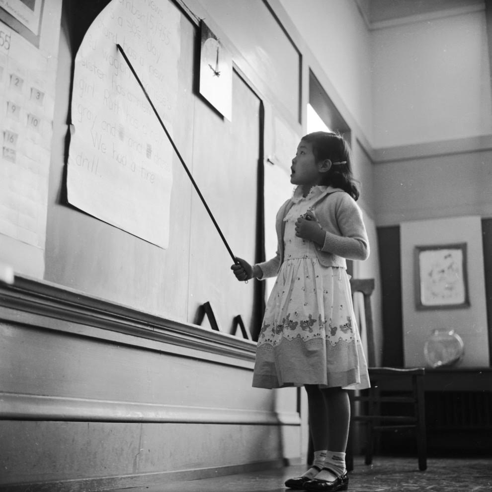 A little girl reads aloud from the blackboard.