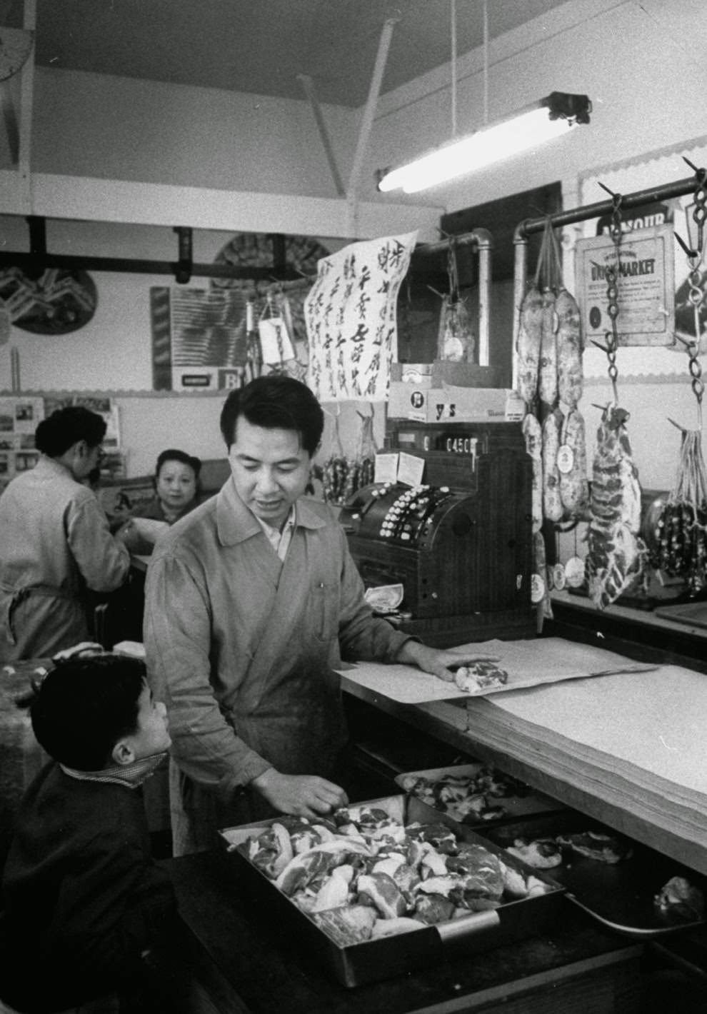 A butcher prepares meat for a young boy.