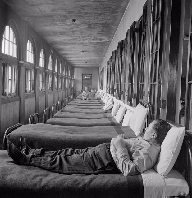 Two men stare out of the windows in a stark hospital ward.