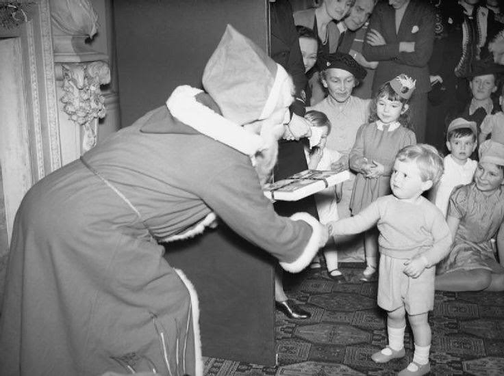 Admiralty Christmas Party for Allied Naval Officers' children, 1942. This photograph shows 'Father Christmas' presenting Winston Churchill Junior, the Prime Minister's grandson, with a gift of a book of nursery rhymes at a Christmas party at Admiralty House.