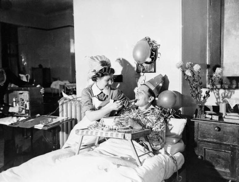 A nurse feeds a patient with a spoonful of Christmas pudding at a naval hospital at Kingseat in Scotland, December 1941.