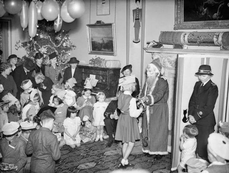 A Christmas party held at Admiralty House, London, 17 December 1942 for allied naval officers children. 'Father Christmas' in a costume and mask presents a young girl with a gift.
