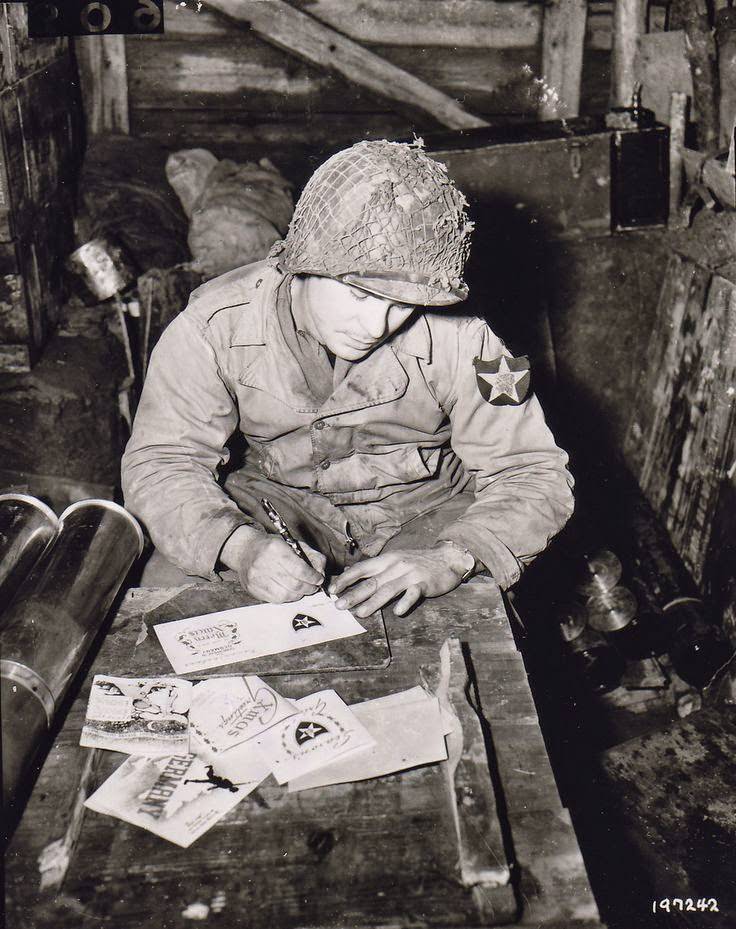 Pvt Walter Prsybyla of B Btry, 37th Field Artillery Regt, US 2nd Inf Div writing Christmas cards for friends and family from an artillery ammunition storehouse, Heckhalenfeld, Germany, 30 Nov 1944.