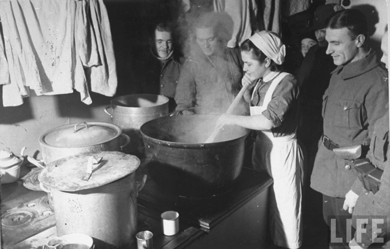 Finnish soldiers watching a woman stirring the pot for Christmas dinner, Finland, 1939.