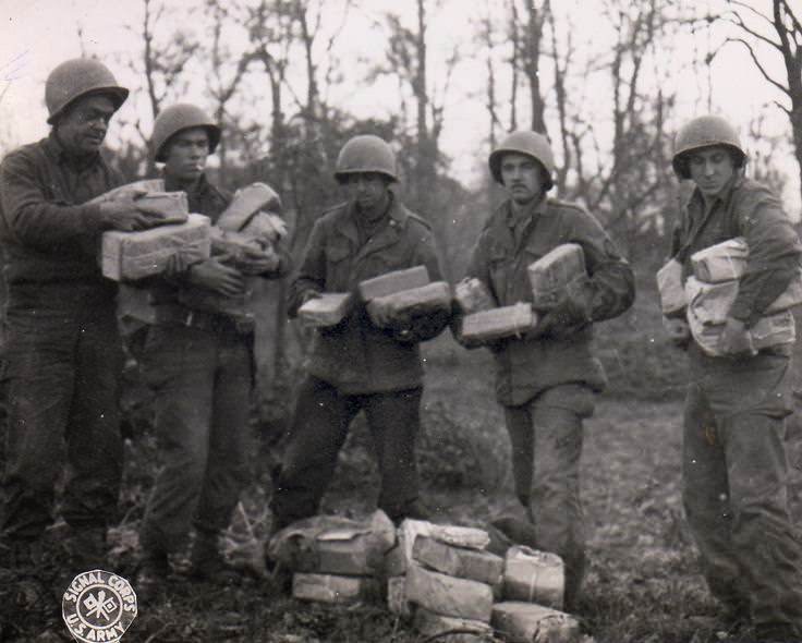 US Army Pfc. W. J. Kessler, Pfc. J. L. Proffitt, Pvt. B. Narter, Cpl. T. J. Barnewski, and Pfc. J. Stoll handling Christmas packages from home for their artillery unit, Germany, 26 Nov 1944.