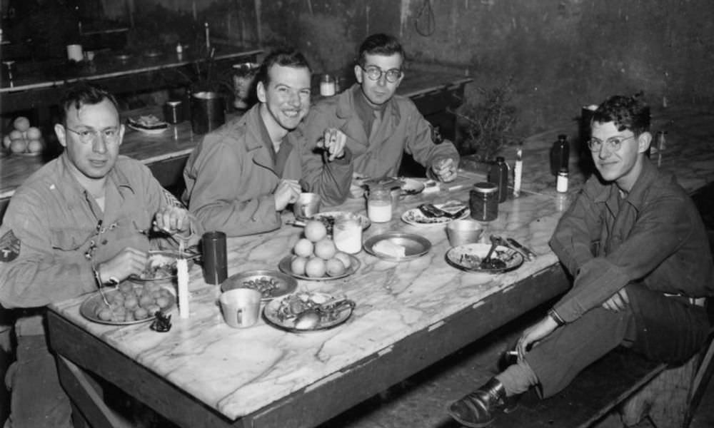 British soldier eating Christmas meal in his slit trench w. holiday cards from home propped up outside, Netherlands, 1944.