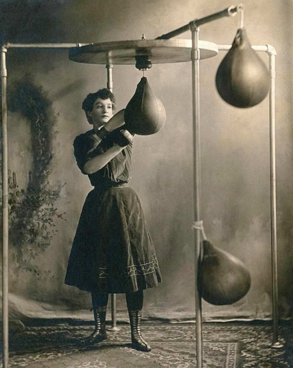 A young woman in a skirt working out with boxing gloves and a punching bag, circa 1890.