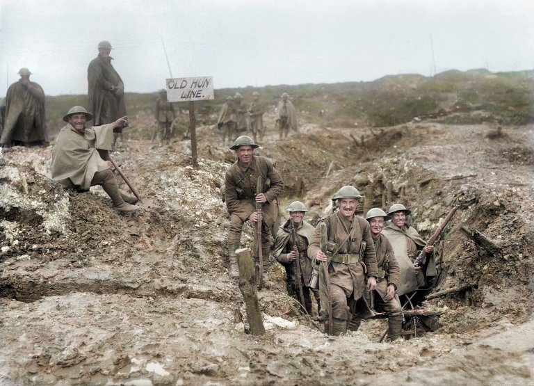 Smiling British men and boys marching out of a trench at captured from the Germans at the Somme. A sign reads 'the old hun line' - referring to where the German front line used to be.