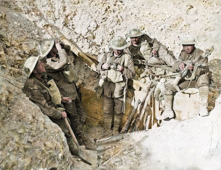 Canadaian soldiers relax in a captured trench in France. One can be seen attending to his rifle as another smokes a cigarette.