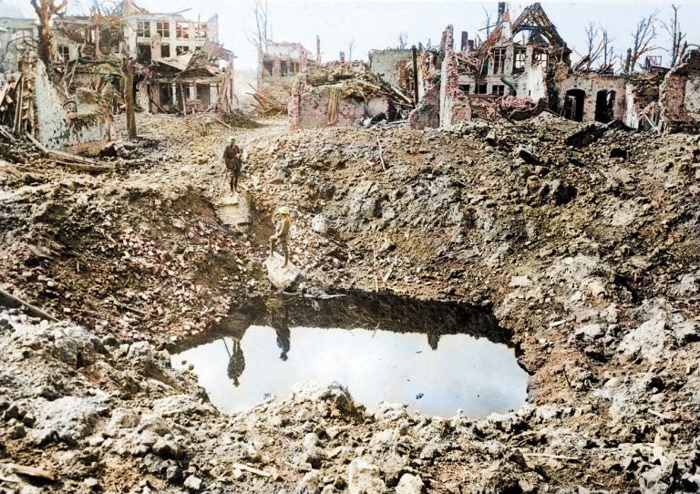 A bombed out town with collapsing buildings as a lone soldier wanders near a crater. Pictured 24. A gigantic shell crater, 75 yards in circumference, Ypres, Belgium, October 1917.