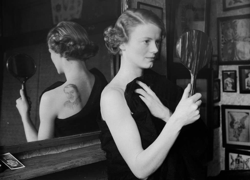 A film fan uses a mirror to admire the image of film star Gary Gooper she has had tattooed on her back by George Burchett a London tattooist, 1936.