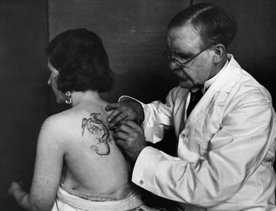 An English woman wearing a pair of elegant crystal earrings is seen getting her first tattoo in 1930.