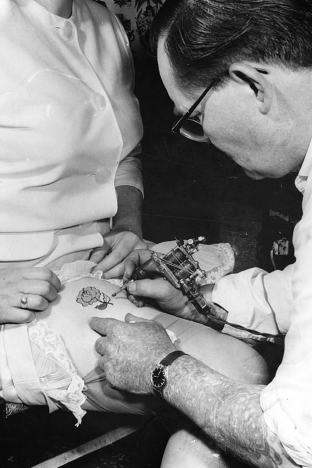 A tattooist paints a small rose on the thigh of a woman in 1961.
