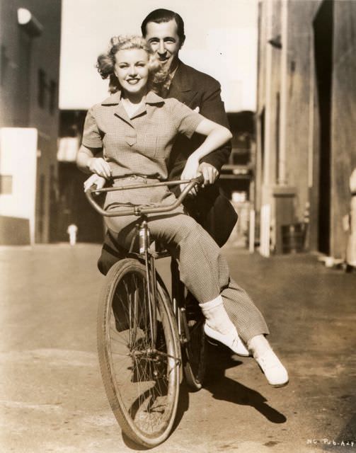 Ann Harding and costume designer Bernard Newmann ride a bike.