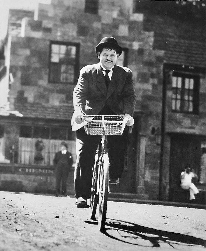 Oliver Hardy riding a bike.