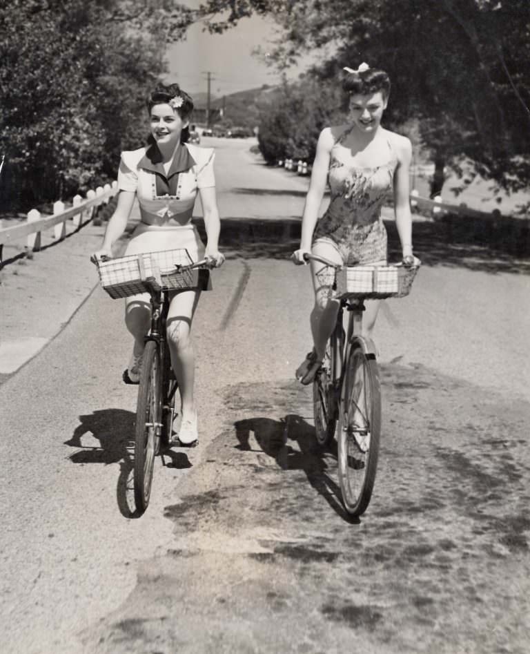 Marguerite Chapman and Leslie Brooks ride bikes.