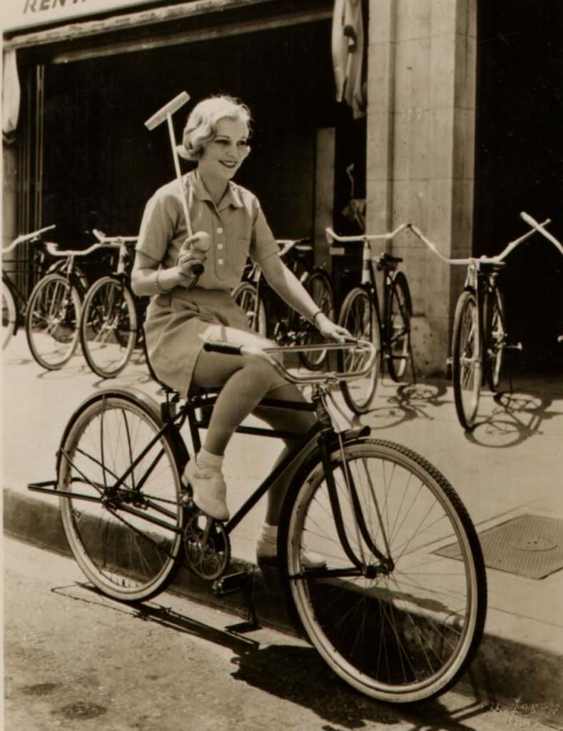 Muriel Evans riding a bike, wields a mallet.