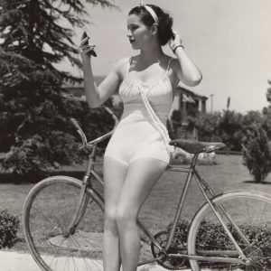 June Travis leans on bike, checks makeup.