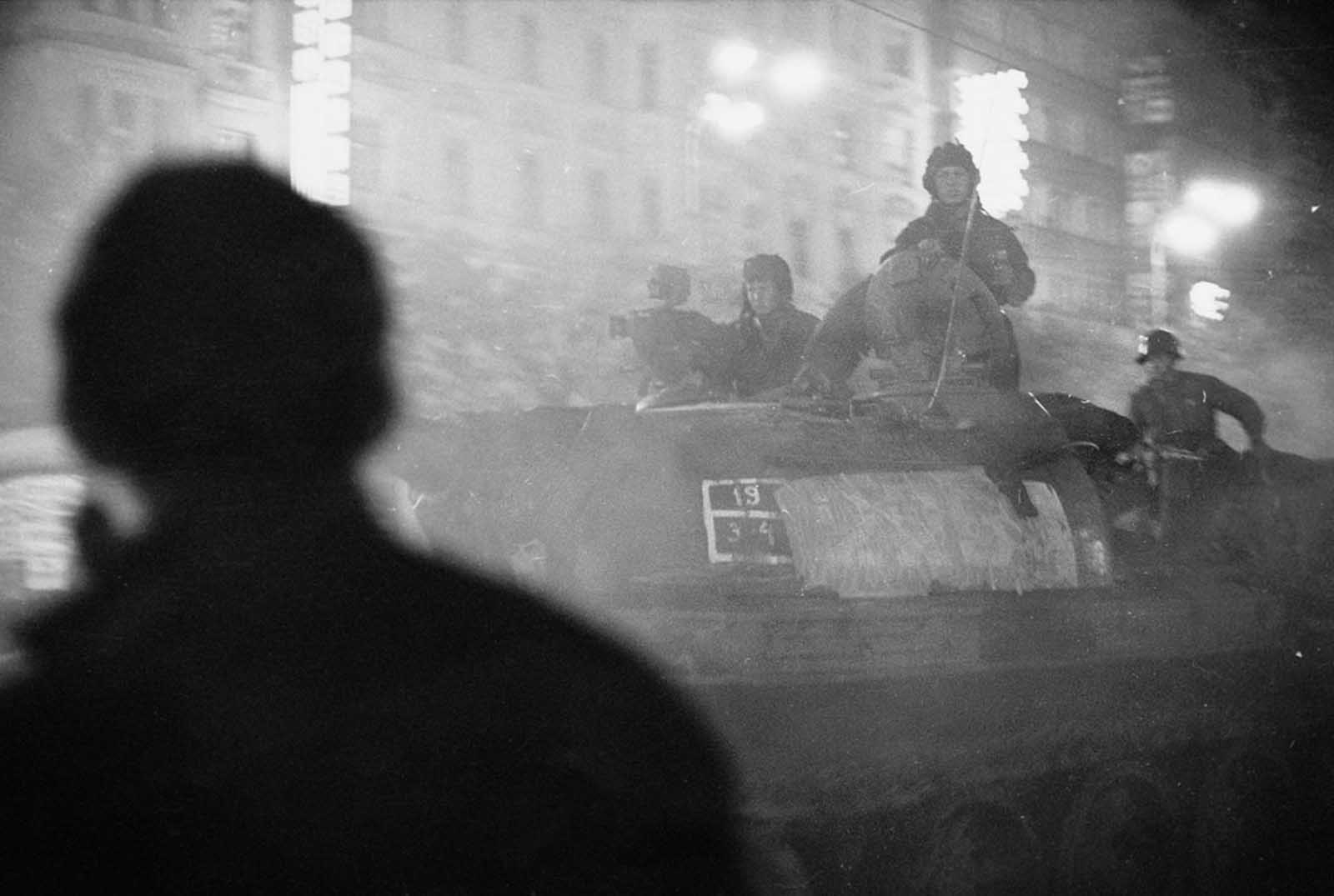 A shadowy figure watches Soviet tanks advance through the streets of Prague after nightfall in August 1968