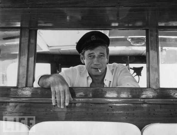 Yves Montand regards his passengers on board his yacht at Cannes during a holiday on the Cote d'Azur on July 28, 1965.