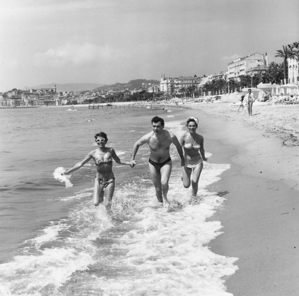 George Baker runs through the surf at Cannes with Bella Darvi and another young friend, 1956.