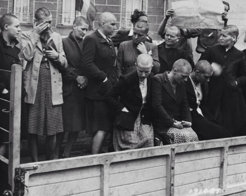 Brutalized women, their heads shaved, are loaded into the back of a truck. The 'man' behind them is holding a sign that says 'collaborators', but who is the real collaborator?