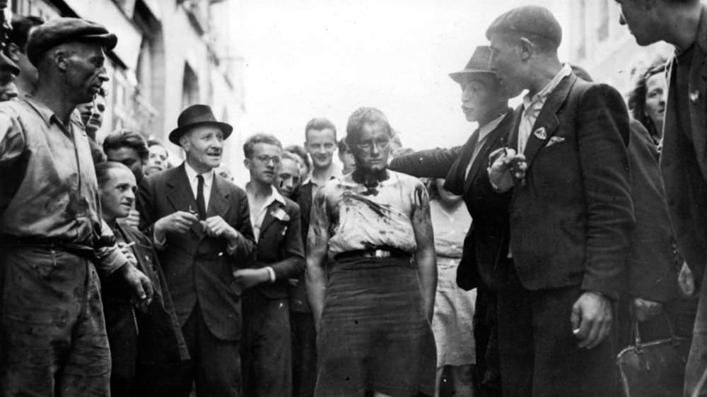 Civilians and members of the French resistance lead a female collaborator through the streets of Rennes after her head was shaven and covered with iodine. August 06, 1944.