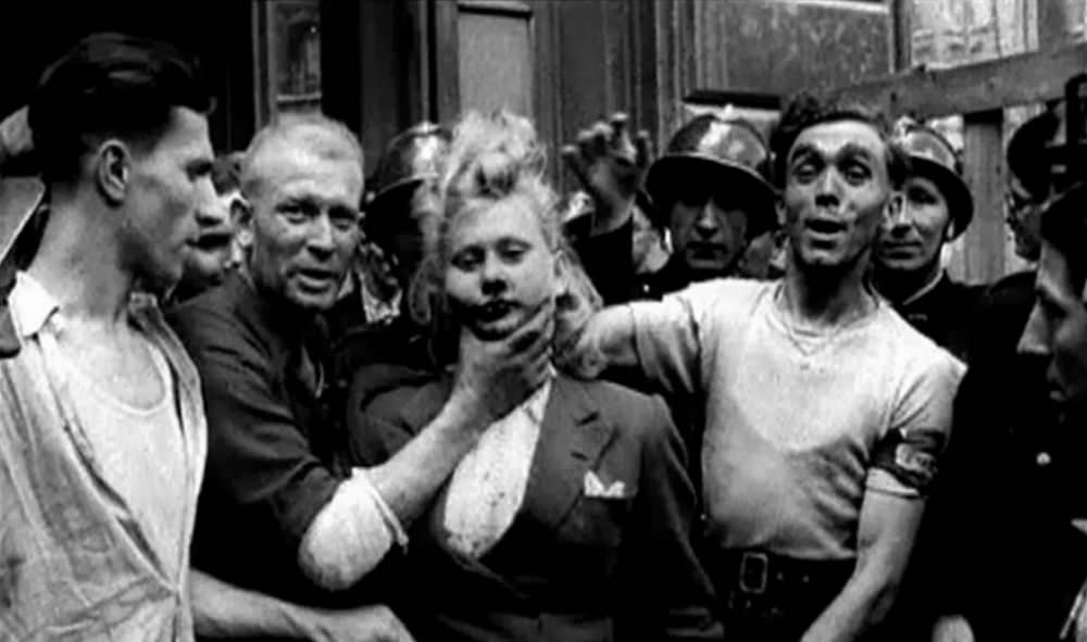 A French woman with a bloody face is forced to look at the camera while French soldiers do nothing.