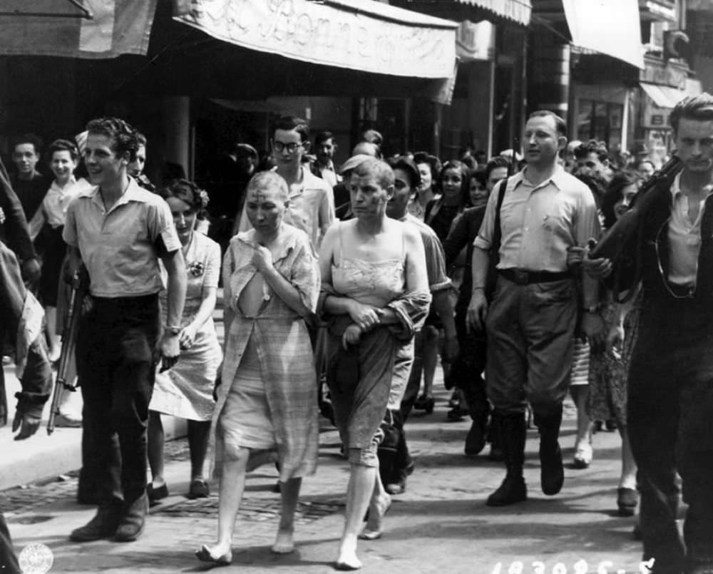 Two women, partially stripped, their heads shaved and with swastikas painted on their faces, are marched barefoot down the streets of Paris, to shame and humiliate them for collaborating with the Germans during the Second World War. August 27, 1944.