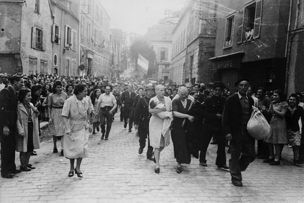 A woman, with her baby whose father is German, and her mother are jeered and humiliated by crowds in Chartres after having their heads shaved as punishment for collaborating with the German troops, 1944.