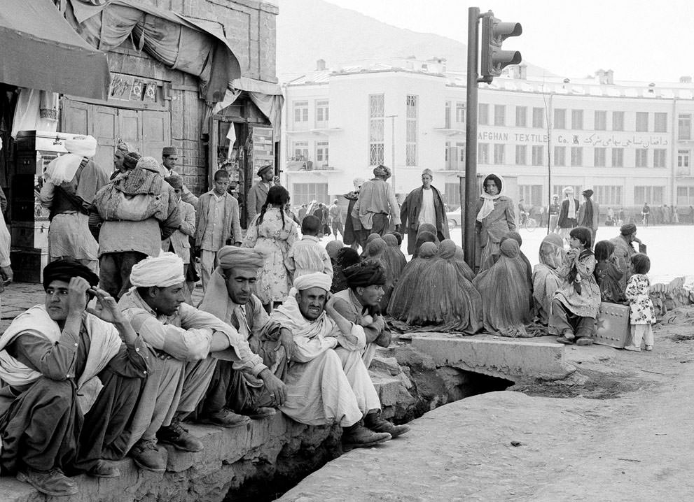 A modern traffic light stands incongruously amid burqa-clad women sitting on a Kabul street corner with their backs to their men on May 25, 1964.