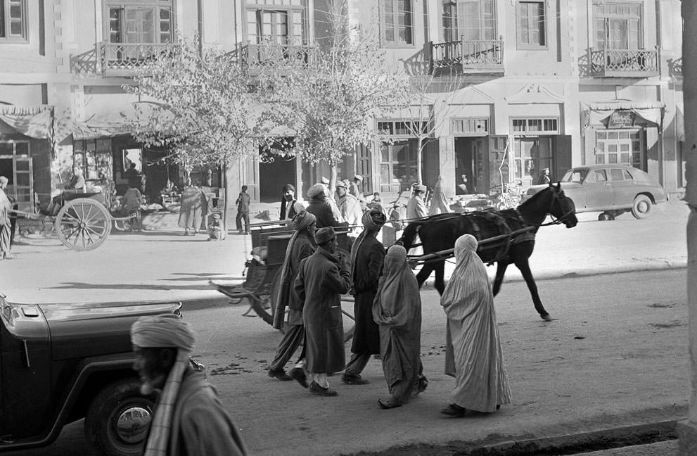 Women, wearing traditional burqas and Persian slippers, walk alongside men, cars and horse carts, in a street in Kabul, in 1951. At the time, this street was one of only three paved streets in the capital city.