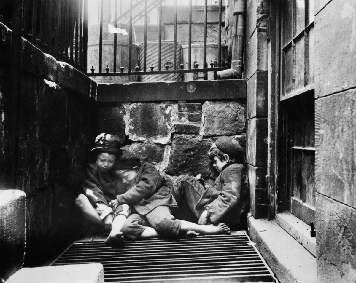 Street children huddle over a grate for warmth on Mulberry Street, 1895