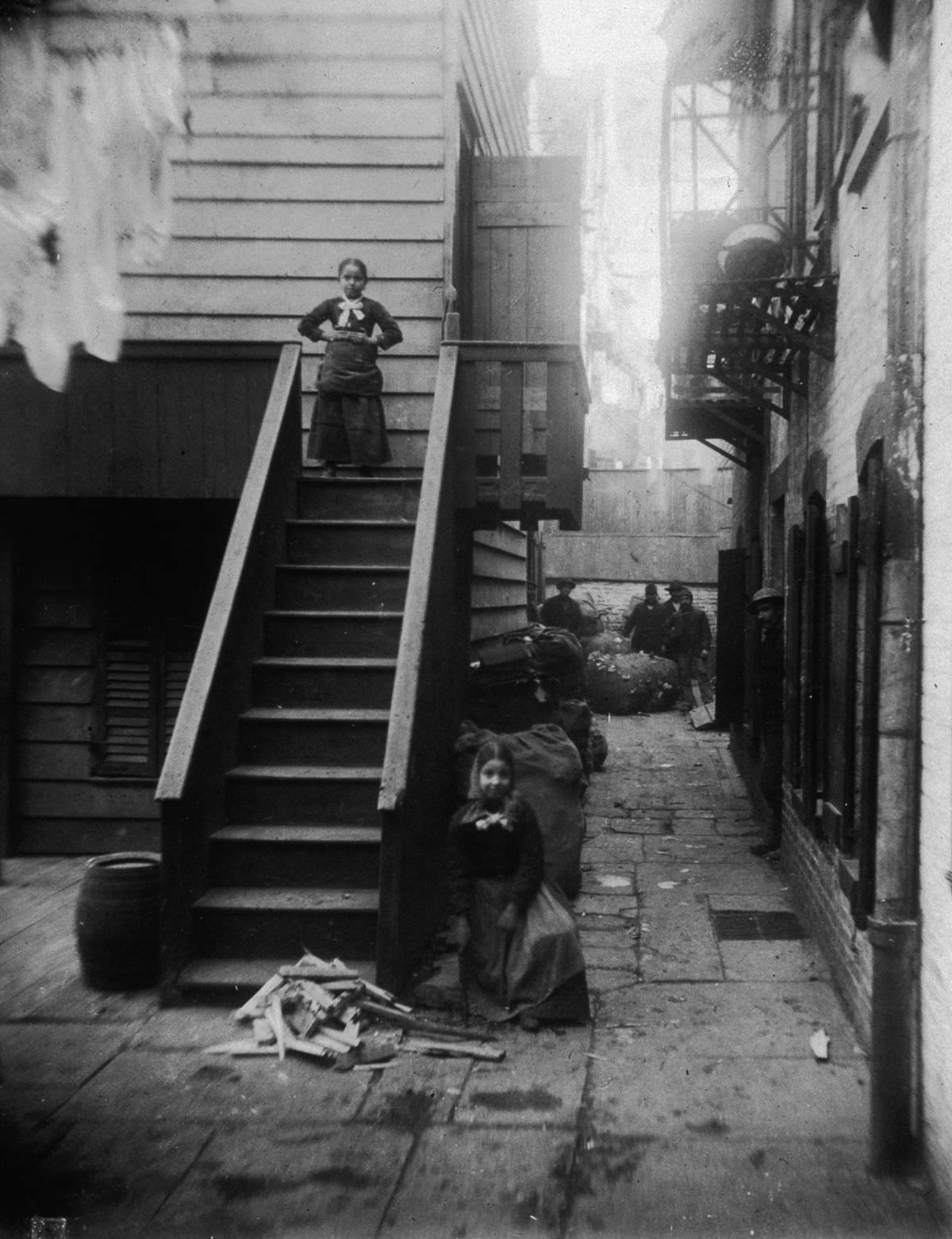 Two young ragpickers stand at a staircase in Baxter Alley, in Little Italy, 1890