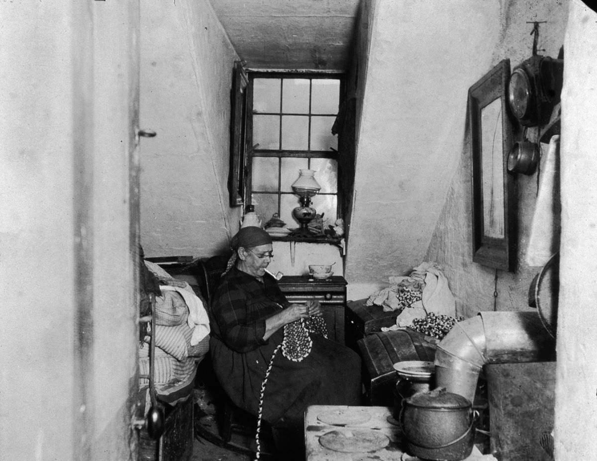 Mrs. Benoit, a Native American widow, sews and beads while smoking a pipe in her Hudson Street apartment, 1897