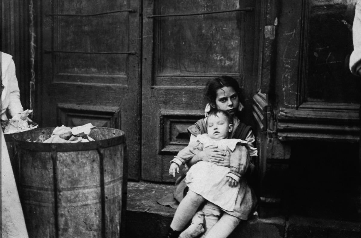 A young girl holds a baby in a doorway, 1890