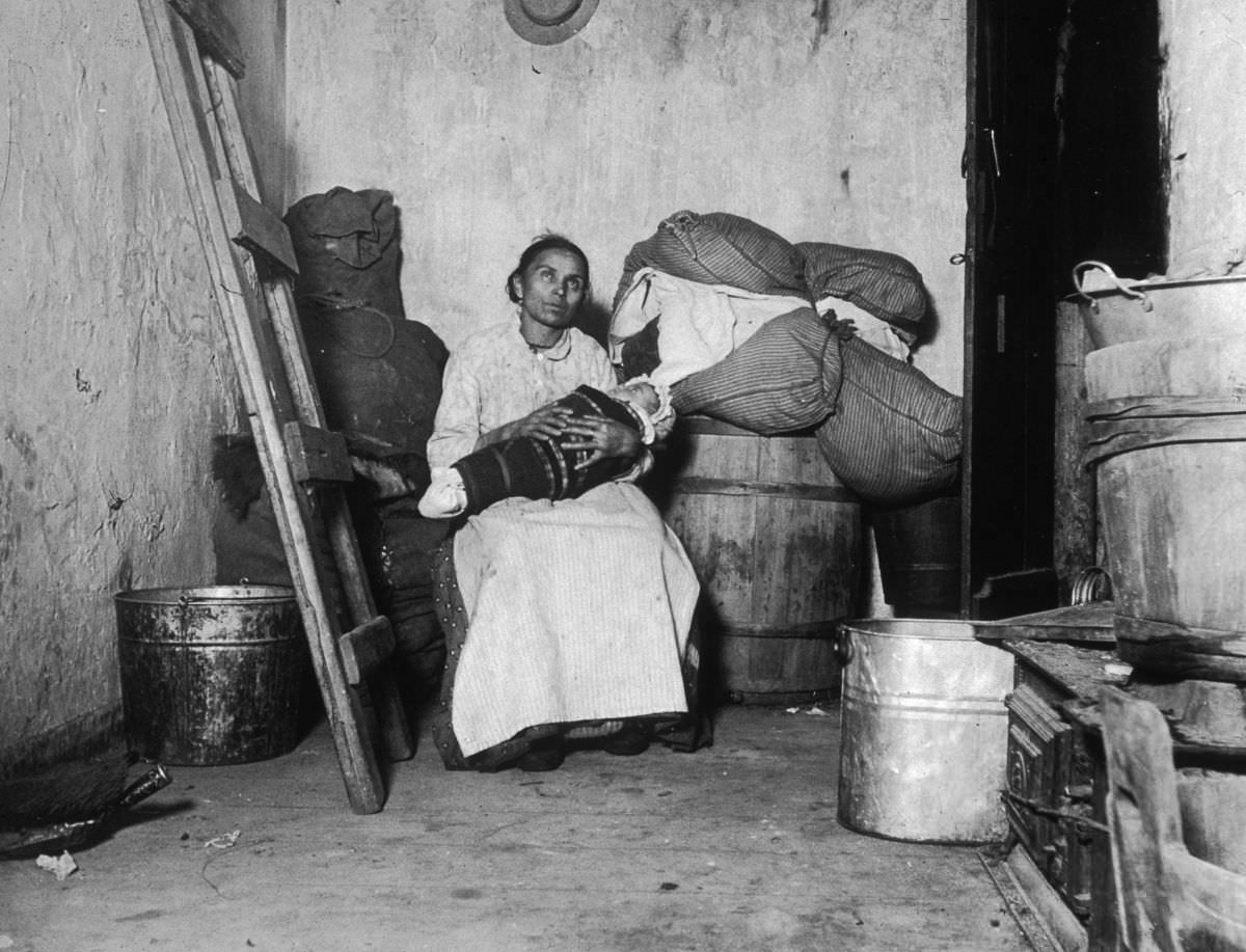An Italian immigrant rag-picker sits with her baby in a small run-down tenement room on Jersey Street, 1887