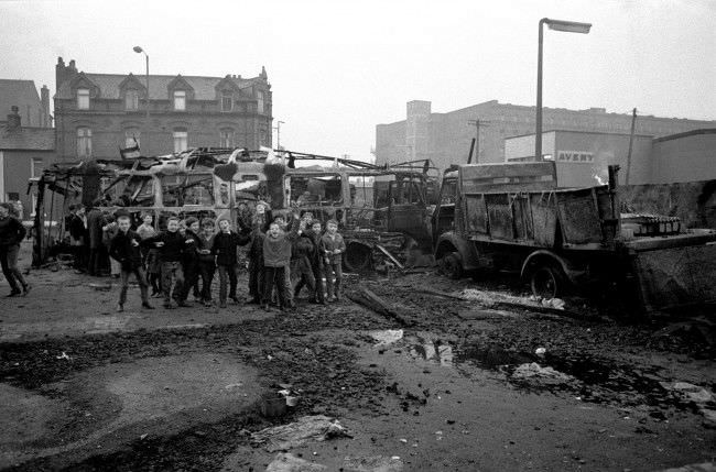 Schoolboys cheer adn chant from a pile of burnt-out busses and lorries in the aftermath of the riots. 9 Feb, 1971