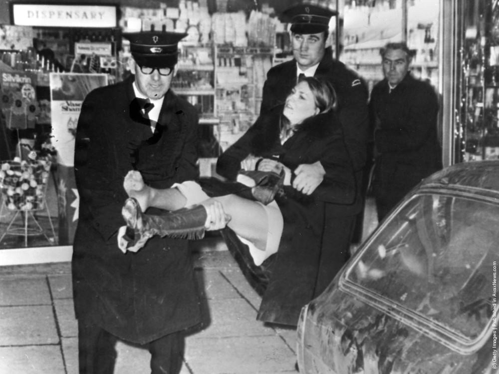 A young woman injured during a shooting incident in Belfast is carried out of a chemists shop by ambulance men, 28th November 1971.